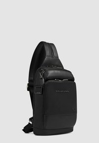 Zaino a tracolla in pelle nera con una texture liscia, dotato di cerniere argentate, una tasca frontale e una tracolla imbottita.