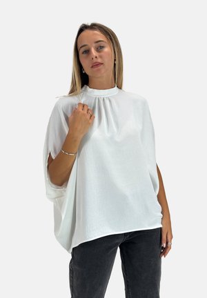 Übergrößige weiße Bluse mit hohem Kragen, strukturiertem Stoff, kurzen Ärmeln und seitlichen Ausschnitten, kombiniert mit dunkelblauen Jeans.