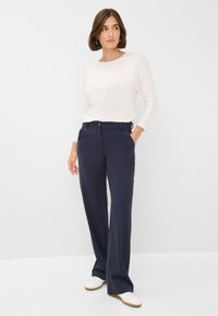 Pantalons larges navy avec passants de ceinture et poches latérales ; assortis à une chemise à manches longues crème. Tissu lisse et coupe ajustée.