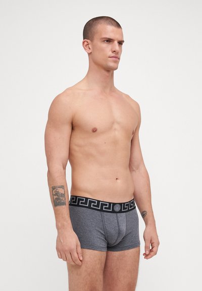 Grå herre-boksershorts med en sort midjebånd som har et gresk nøkkelmønster. Materialet ser mykt ut, og gir en tettsittende passform og definert silhuett.
