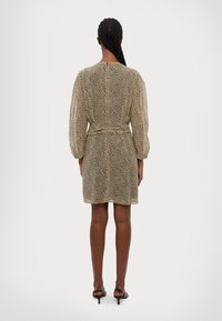 Šaty s krátkym rukávom v krémovo-čiernom bodkovanom vzore, s priliehavým pásom, splývavou tkaninou a dĺžkou do kolien.