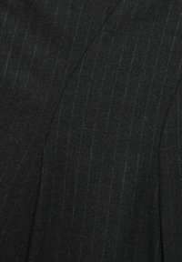 Tissu noir avec de subtils rayures fines. Texture lisse avec une légère brillance. Le matériau semble lourd et taillé pour un ajustement structuré.