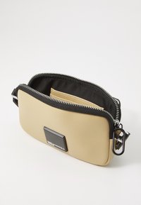 Beiger Handytasche aus Kunstleder mit schwarzem Reißverschluss, silbernen Beschlägen und einem Logoplatte. Das Innere ist mit einem schwarzen Futter versehen und verfügt über mehrere Taschen.