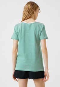 Stribet grøn t-shirt med korte ærmer, rund halsudskæring og hvid kant. Lavet af letvægtsstof, har vandrette striber.