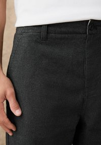 Close-up of person wearing dark gray pinstriped trousers with a button closure, paired with a white top.