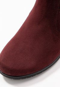 Burgundowe zamszowe botki za kostkę z zaokrąglonym noskiem, teksturowaną cholewką i czarną gumową podeszwą. Ozdobione subtelnym przeszyciem wzdłuż krawędzi.