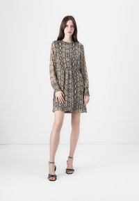 Beige klänning med ormskinnsmönster, långa ärmar, samlad midja och genomskinligt tyg. Matchad med svarta klacksandaler med prickiga detaljer.