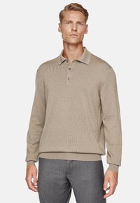 Polo shirt beige a maniche lunghe con texture a costine, colletto a polo e chiusura con tre bottoni. Abbinato a pantaloni grigi.