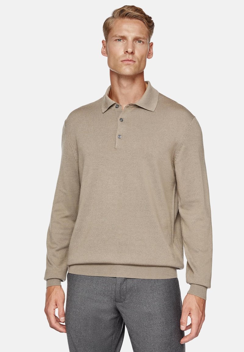 Polo shirt beige a maniche lunghe con texture a costine, colletto a polo e chiusura con tre bottoni. Abbinato a pantaloni grigi.