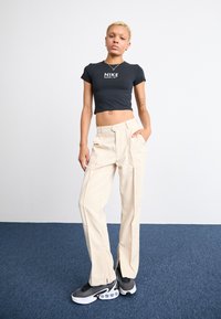 Svart avkortet skjorte med "Nike"-logo, beige cargo-bukser med lommer, og svarte sneakers med teksturert overdel og synlig luftdempering.