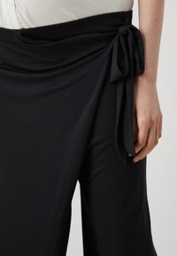 Μαύρη φούστα ντύματος από απαλό, ρέον ύφασμα. Διαθέτει φιόγκο στη μέση, δημιουργώντας ένα εφέ ρούχου με λεία υφή.