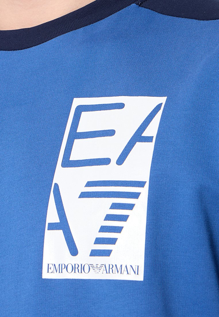 Camiseta de poliéster azul con cuello redondo, que presenta un audaz gráfico en blanco del logo "EA7" y "EMPORIO ARMANI" en el pecho.