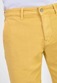 Chinos jaunes en coton, avec une coupe classique, une fermeture éclair et un bouton. Texture lisse avec des poches latérales standard.