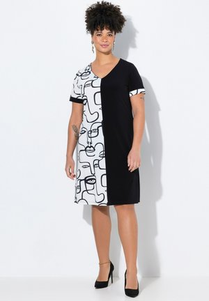 Kurzärmliges Kleid mit V-Ausschnitt, das eine schwarze Seite und eine weiße Seite mit abstrakten Gesichtsmustern aufweist. Hergestellt aus weichem, dehnbarem Stoff.