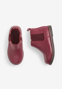 Botas de tobillo de cuero burdeos con paneles laterales elásticos, perforaciones decorativas y una suela de goma marrón. Cremallera en la parte trasera para una fácil colocación.