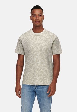 Man wearing beige floral-patterned short-sleeve t-shirt and light blue denim jeans against a plain white background.