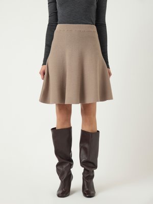 Jupe beige évasée en tissu mélangé de laine texturé, avec une taille ajustée. Associée à des bottes en cuir marron foncé mi-mollet.