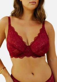 Soutien-gorge en dentelle rouge avec des motifs floraux, des bords festonnés et des bretelles ajustables. Caractérisé par un fermoir décoratif au centre. Texture douce.