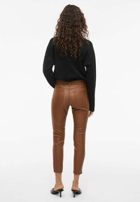 Brązowe spodnie z ekoskóry o slim fit, z wysokim stanem, kieszeniami naszytymi i gładką powierzchnią, w połączeniu z czarnym swetrem.