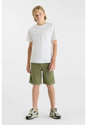 Adolescent portant un T-shirt blanc à manches courtes, un short kaki vert jusqu'au genou, et des baskets noir et blanc, debout devant un fond blanc.