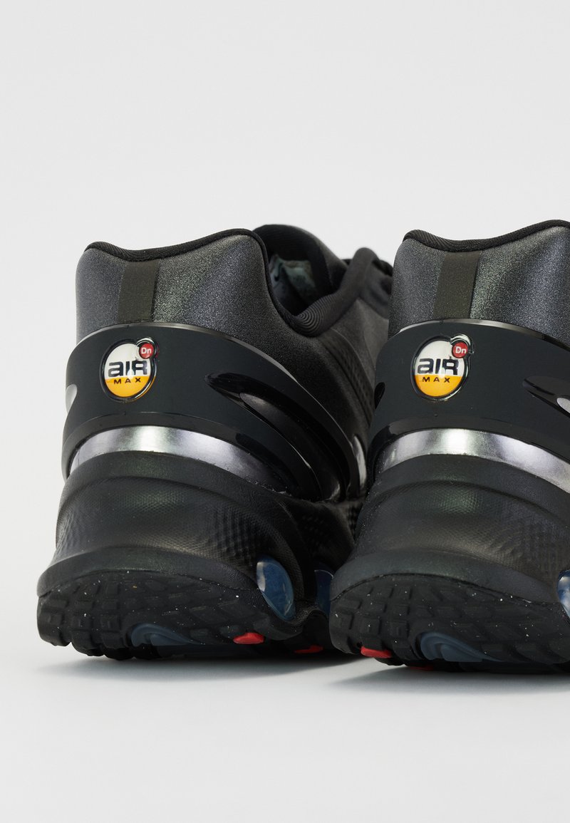 Zapatos deportivos negros con parte superior de textil suave, acentos reflectantes y suela acolchada con unidades de aire visibles y una banda de rodadura texturizada.