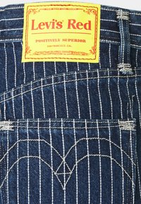 Levi's Red label attached to blue denim with white vertical stripes, featuring heart-shaped stitching and a distinctive rectangular tag.