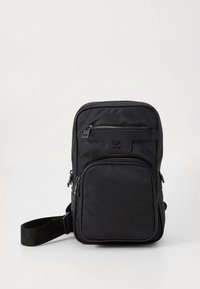 Black nylon crossbody bag with two zippered compartments and an adjustable strap. Features a subtle logo on the front panel and smooth texture.