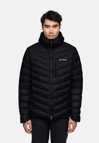 Giubbotto piumino nero con trapuntatura a zig zag, chiusura lampo frontale, colletto alto e logo sul petto. Design leggero e isolato.