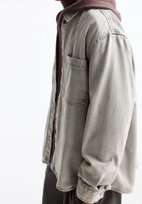 Jasnoszara koszula dżinsowa z długimi rękawami, zapięcie na guziki i kieszonka na piersi. Na to nałożona bordo bluza z kapturem.