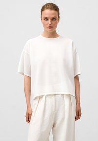 Witte cropped sweatshirt met korte mouwen, ronde halslijn en textuurstof. Gepaard met lichte, losse broeken.