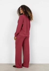 Bordeauxrode sweatshirt en bijpassende wijde broek van zachte stof. De outfit heeft een ontspannen pasvorm en geribbelde boorden, met een ronde halslijn.