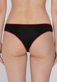 String noir en coton avec un bord festonné rouge. Présente une coupe basse et une texture lisse et extensible. Design à couverture minimale.