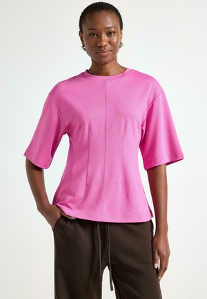 Lyserød kortærmet bluse med en afslappet pasform, der har en rund halsudskæring og lodrette sømdetaljer på forsiden. Glat, let stof.