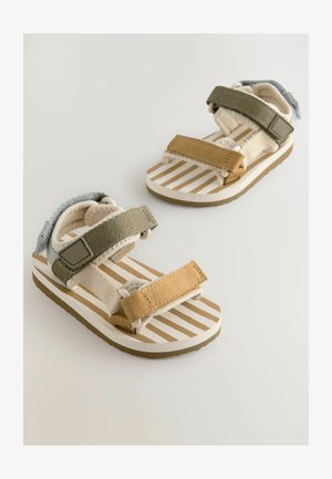 Sandali con cinturini in beige e verde con suole a motivi a righe. Presentano cinturini in tessuto regolabili e una soletta testurizzata. Suola in gomma.