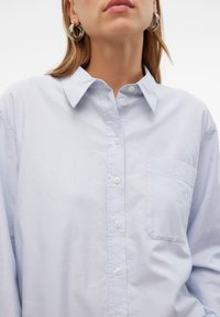 Camicia azzurra chiaro con colletto a punta, maniche lunghe e taschino sul petto. Realizzata in tessuto morbido con una texture liscia.