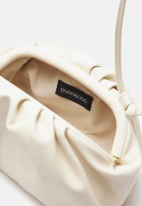 Bolso de mano de imitación cuero blanco con diseño arrugado, textura suave y una etiqueta en el interior. Presenta un forro beige y un cierre de cremallera dorado.