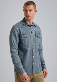 Jasnoniebieska koszula dżinsowa, z długimi rękawami, zatrzaskami, dwiema kieszeniami na piersi oraz detalami w stylu zachodnim na karczku. Gładka tekstura i luźny fason.
