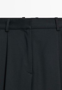 Black dress pants featuring a flat front, sharp pleats, and a smooth, textured fabric. Waistband with belt loops and side pockets.