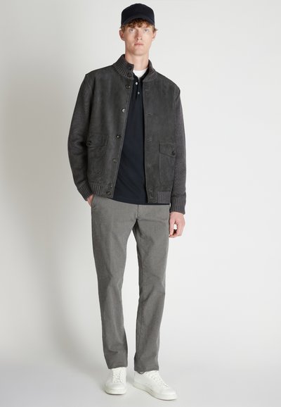 Giacca in pelle e maglia con un design a blocchi di colore grigio, due tasche frontali, indossata su un polo nero, abbinata a pantaloni grigi e sneaker bianche.