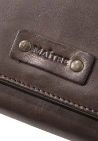 Bruine leren zak met een textuur oppervlak, voorzien van een metalen drukknoop en een geperst label "MAÎTRE." Zichtbare stiksels langs de rand.