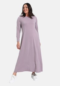 Langärmliges, bodenlanges Kleid aus pastell-lavendelfarbenem Stoff, mit einem schlichten Design, kombiniert mit weißen Sneakers. Glatte Textur, keine Muster.