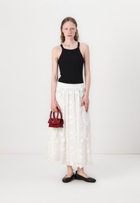 Zwarte mouwloze top, witte gestructureerde rok met bloemmotieven, rode handtas en zwarte platte schoenen. Eenvoudige en elegante outfit.