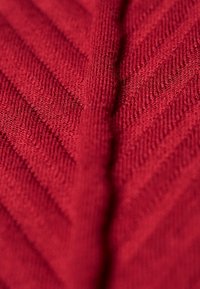 Rotes Strickgewebe mit einem strukturierten Fischgrätmuster, das erhöhte diagonale Linien und eine weiche, glatte Oberfläche aufweist.