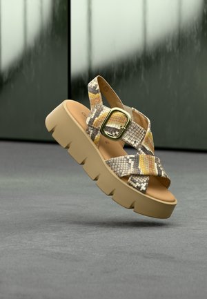Plateauzandalen met gekruiste bandjes in geel, bruin en zwarte slangenprint. Stevige beige zool met metalen gespsluiting.