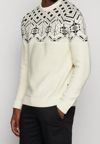 Crème brei trui met een zwart geometrisch patroon op de bovenkant en ribgebreide manchetten en zoom. Casual fit met ronde halslijn.