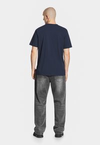 Granatowa bawełniana koszulka z klasycznym okrągłym dekoltem, w połączeniu z luźnymi szarymi dżinsami z wyblakłą texturą i przeszyciami z denimu.