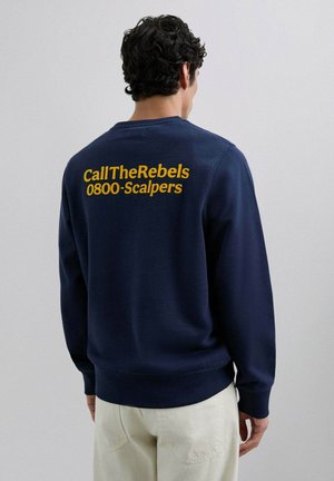 Sudadera de color azul marino hecha de una tela suave, con gran texto amarillo en la parte posterior: "CallTheRebels 0800-Scalpers". Cuello redondo simple.
