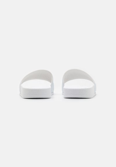 Vita skidsandaler i vitt med en slät, texturerad fotbädd, öppen tådesign och platt sula. Minimalistisk estetik med kurviga, stödjande remmar.
