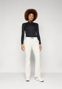 Μακρυμάνικη μαύρη μπλούζα με ψηλό λαιμό, συνδυασμένη με λευκό παντελόνι με καμπάνα. Συμπληρώστε την εμφάνιση με λευκά αθλητικά παπούτσια και μεταλλική ζώνη.