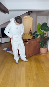 Bela kapuca s centralnim logotipom, bele široke hlače i srebrni tenisice. Unutarnji prostor s smeškom od smešnog materijala i biljkom.